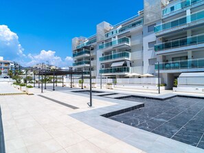 Un immeuble résidentiel moderne à plusieurs étages, doté de balcons, d’une terrasse sur le toit et d’un espace piscine.
