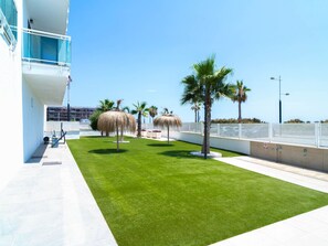 A well-maintained outdoor area with a grassy lawn, palm trees, and a building with a blue balcony. - Apartment  by Interhome (Torrox Costa)