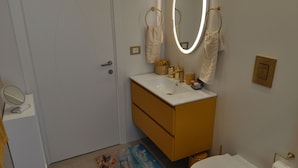 A bathroom with a toilet, sink, and mirror. There is a door, a rug, and a towel rack. - Romeo House (Cagliari)