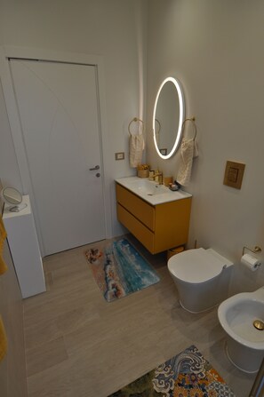 A bathroom with a toilet, sink, and mirror. There is a door, a rug, and a towel rack. - Romeo House (Cagliari)
