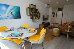 A dining area with a white table, yellow chairs, and a painting of a surfer on a wave. - Romeo House (Cagliari)