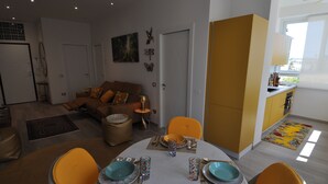 A modern living room with a sofa, dining table set for two, and a kitchen area with yellow cabinets. - Romeo House (Cagliari)