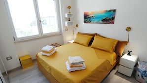 A bedroom with a bed, pillows, a nightstand, a lamp, a painting, and a window. - Romeo House (Cagliari)