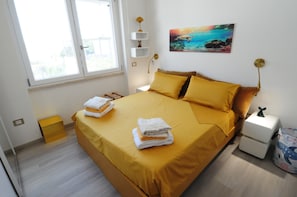 A bedroom with a bed, pillows, a nightstand, a lamp, a painting, and a window. - Romeo House (Cagliari)