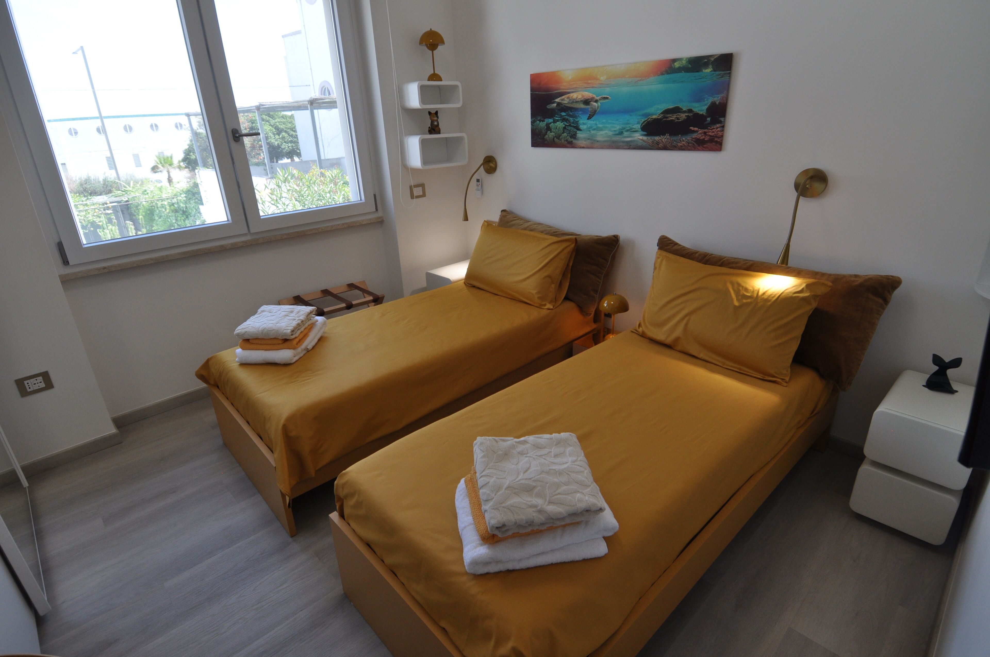 A hotel room with two beds, a window, a painting, and a nightstand.
