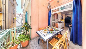 Un pequeño espacio al aire libre con comedor, mesa lista para dos personas, rodeado de plantas en macetas y vista a la calle.