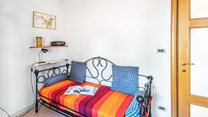 Una habitación pequeña con una cama, un estante con una radio, una lámpara y una puerta.