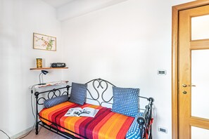 Ein kleines Zimmer mit einem Bett, einem Regal mit einem Radio, einer Lampe und einer Tür.
