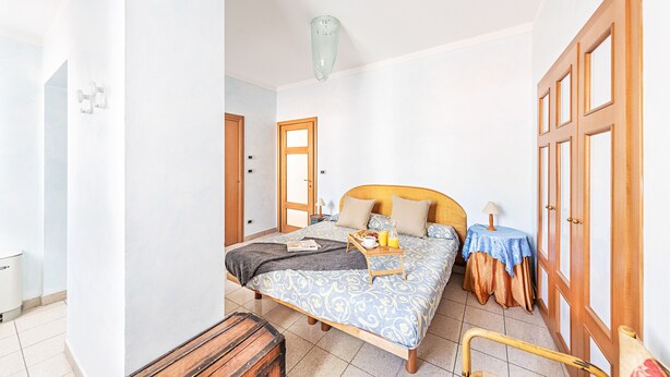 Un dormitorio con una cama, mesitas de noche, un banco de madera y una puerta.