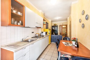 A compact kitchen with white cabinets, a gas stove, and a sink. There's a dining area with a table and chairs, and a small refrigerator. - Gaudio Flat near Ariston Theater by Wonderful Italy (Sanremo)