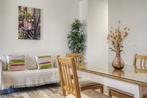 Ein modernes Wohnzimmer mit einem Esstisch mit Glasplatte, Holzstühlen, einem gestreiften Sofa und einem Blumentopf.