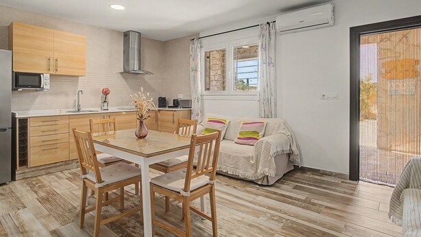 A modern kitchen with wooden cabinets, a dining table with chairs, and a sofa. - Holiday Home 'El Islote del Sur' with Private Pool, Wi-Fi & Air Conditioning (Conil de la Frontera)