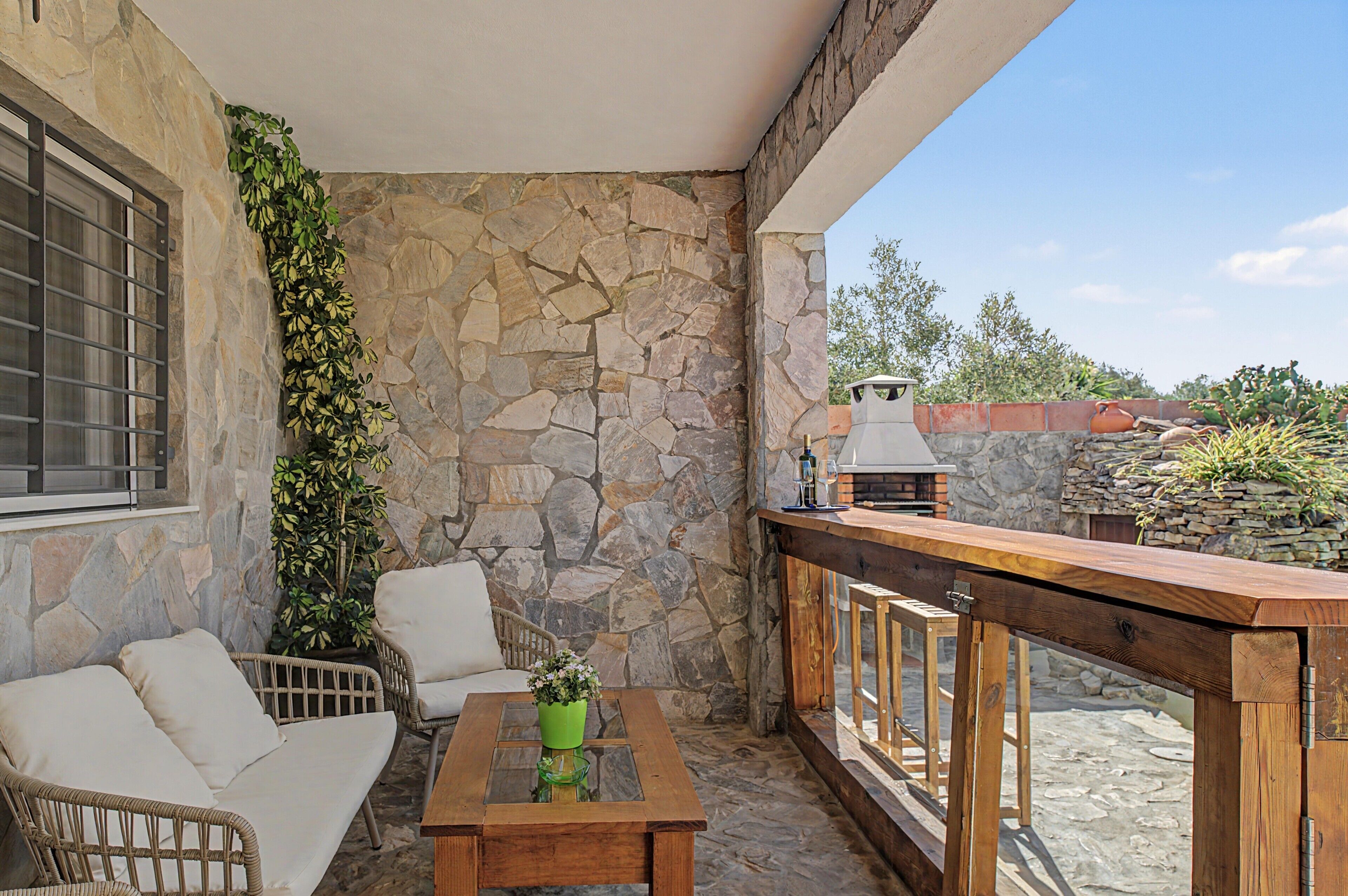 Eine Terrasse mit Steinwänden, Gartenmöbeln, einem Holztisch und einem Grill.