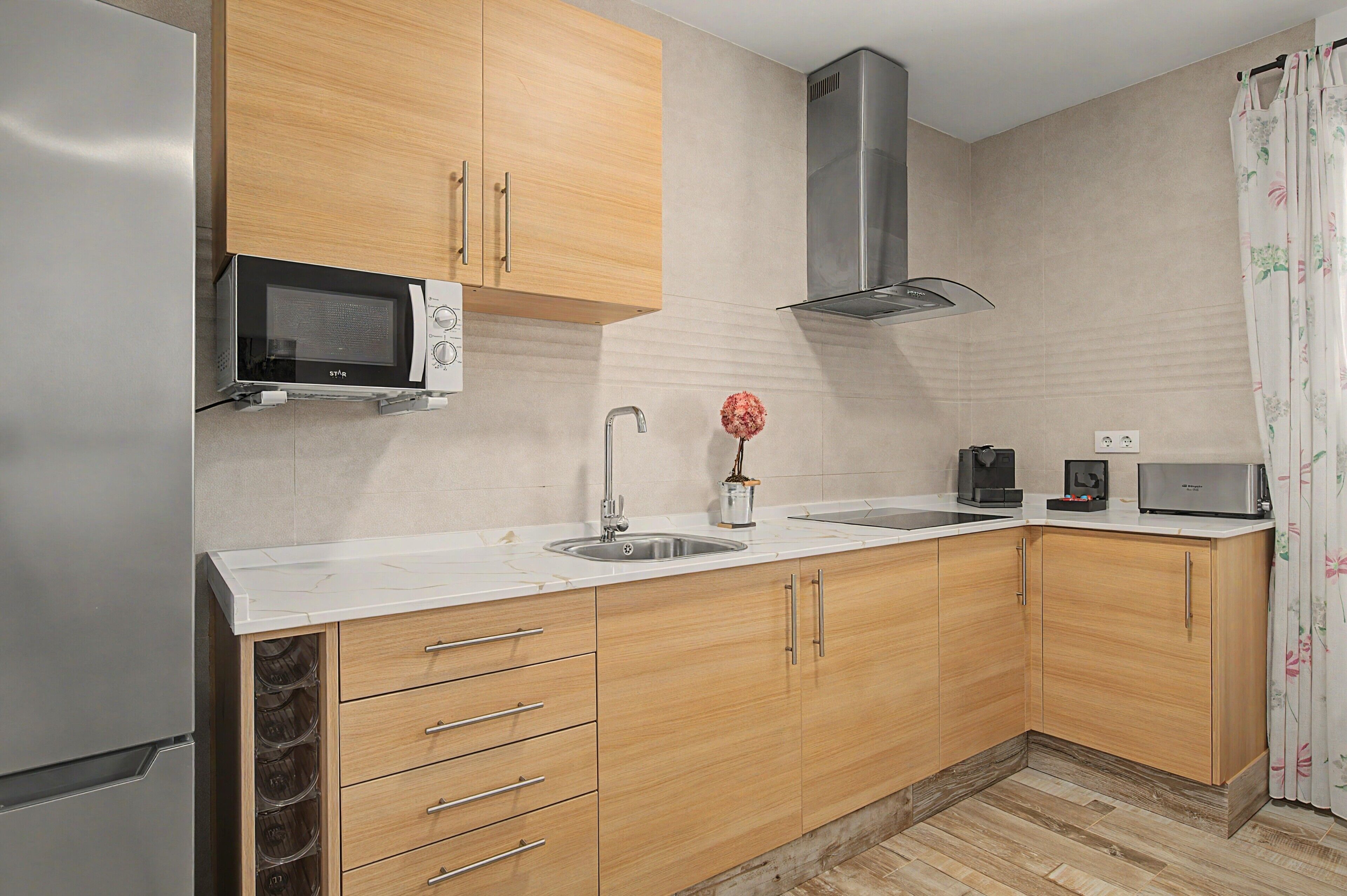 Una cocina moderna con armarios de madera, un lavamanos de acero inoxidable, un microondas y una campana extractora.