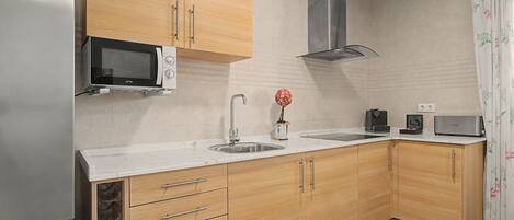Una cocina moderna con armarios de madera, un lavamanos de acero inoxidable, un microondas y una campana extractora.