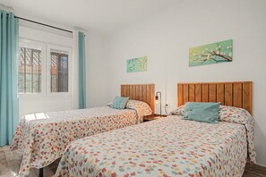 Ein Schlafzimmer mit zwei Betten, einem Fenster mit Vorhängen und zwei Wandbildern.