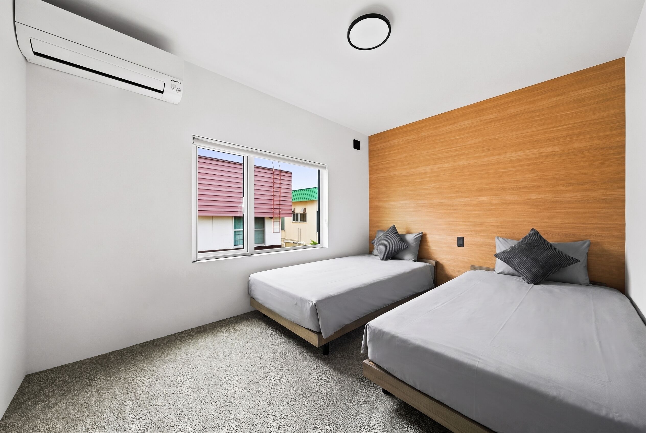 A hotel room with two beds, a window with blinds, an air conditioning unit, and a wooden headboard.