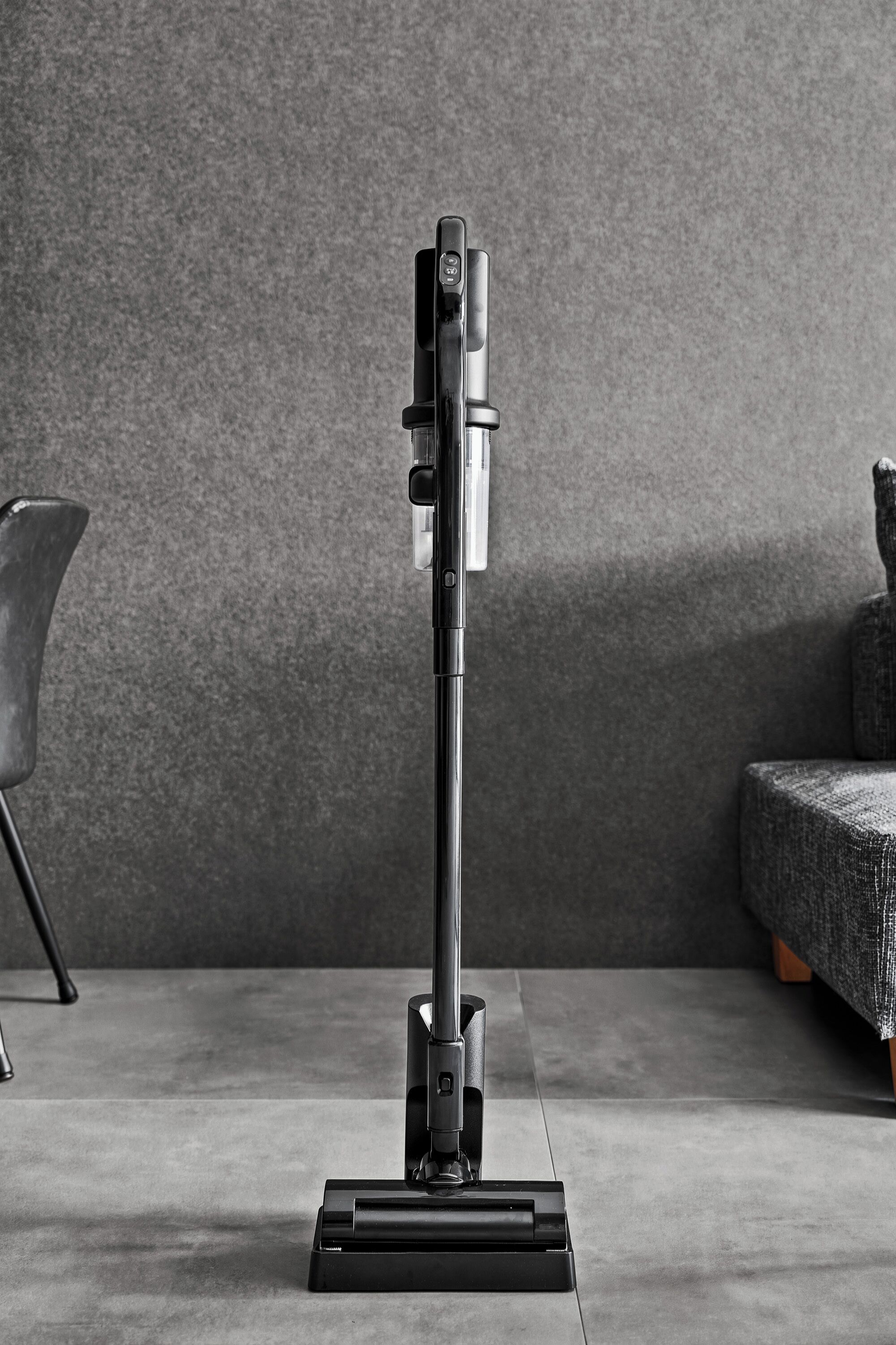 A vacuum cleaner on a flat surface with a textured wall and a chair in the background.