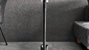 A vacuum cleaner on a flat surface with a textured wall and a chair in the background.