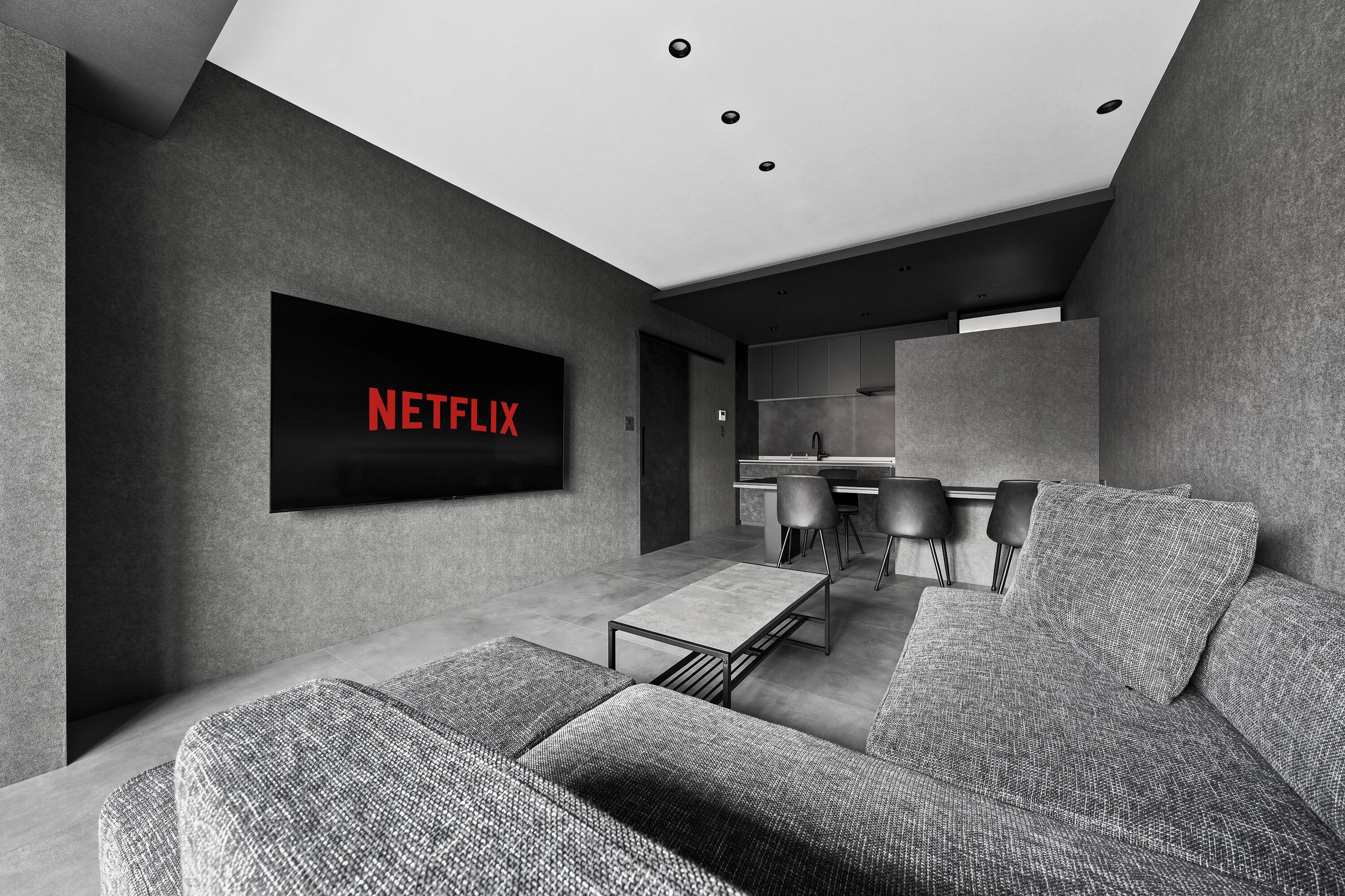 Un salon moderne doté d’un téléviseur à écran plat fixé au mur, d’un canapé, d’une table basse et d’un coin repas avec des chaises.