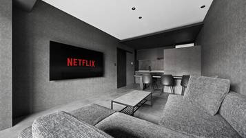 Un salon moderne doté d’un téléviseur à écran plat fixé au mur, d’un canapé, d’une table basse et d’un coin repas avec des chaises.