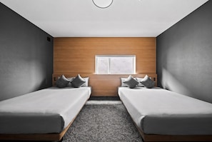 Una habitación con dos camas individuales, un cabecero de madera, un ventanal pequeño y una alfombra con textura.
