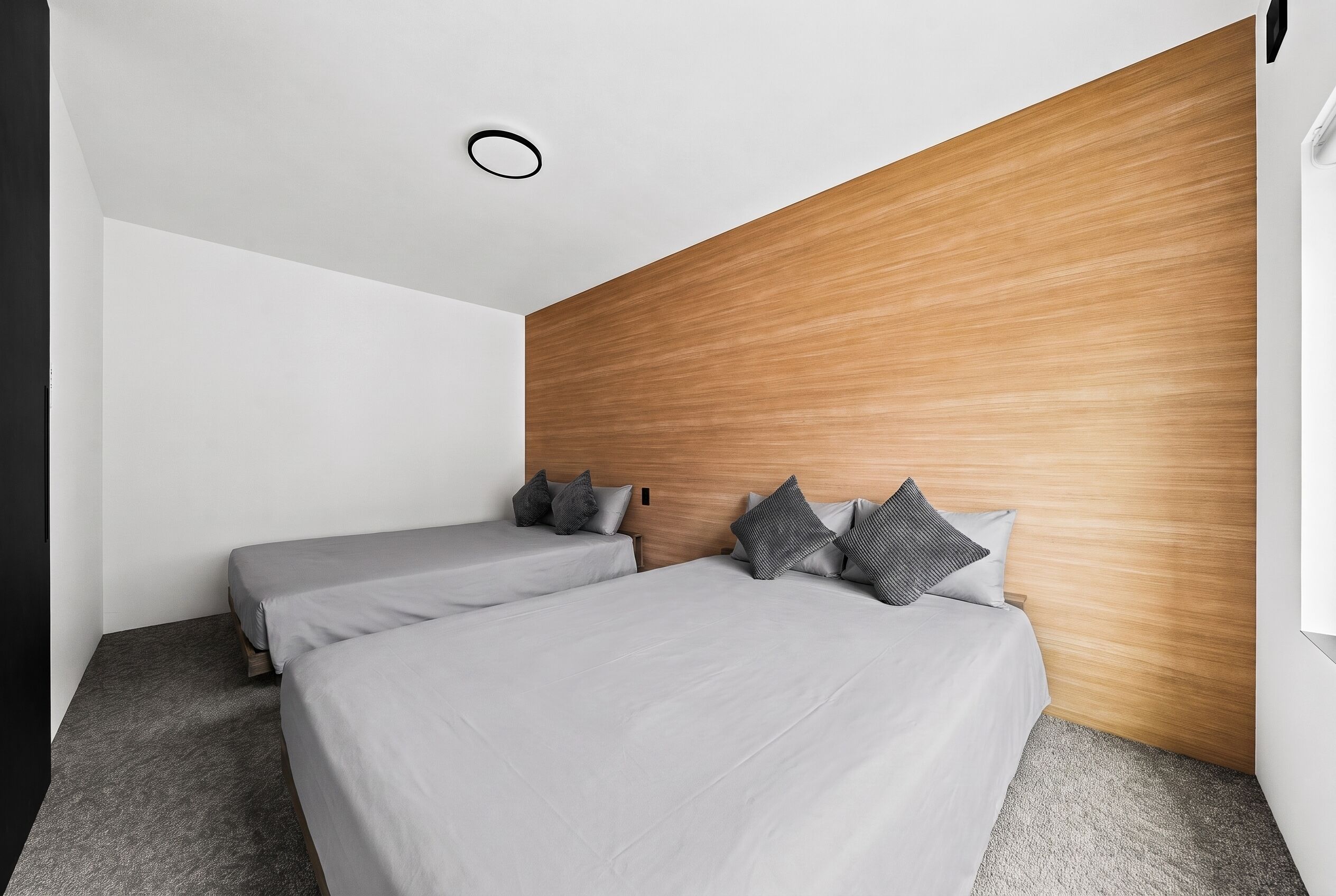 A modern hotel room with two beds, a wooden accent wall, and a simple, clean design.