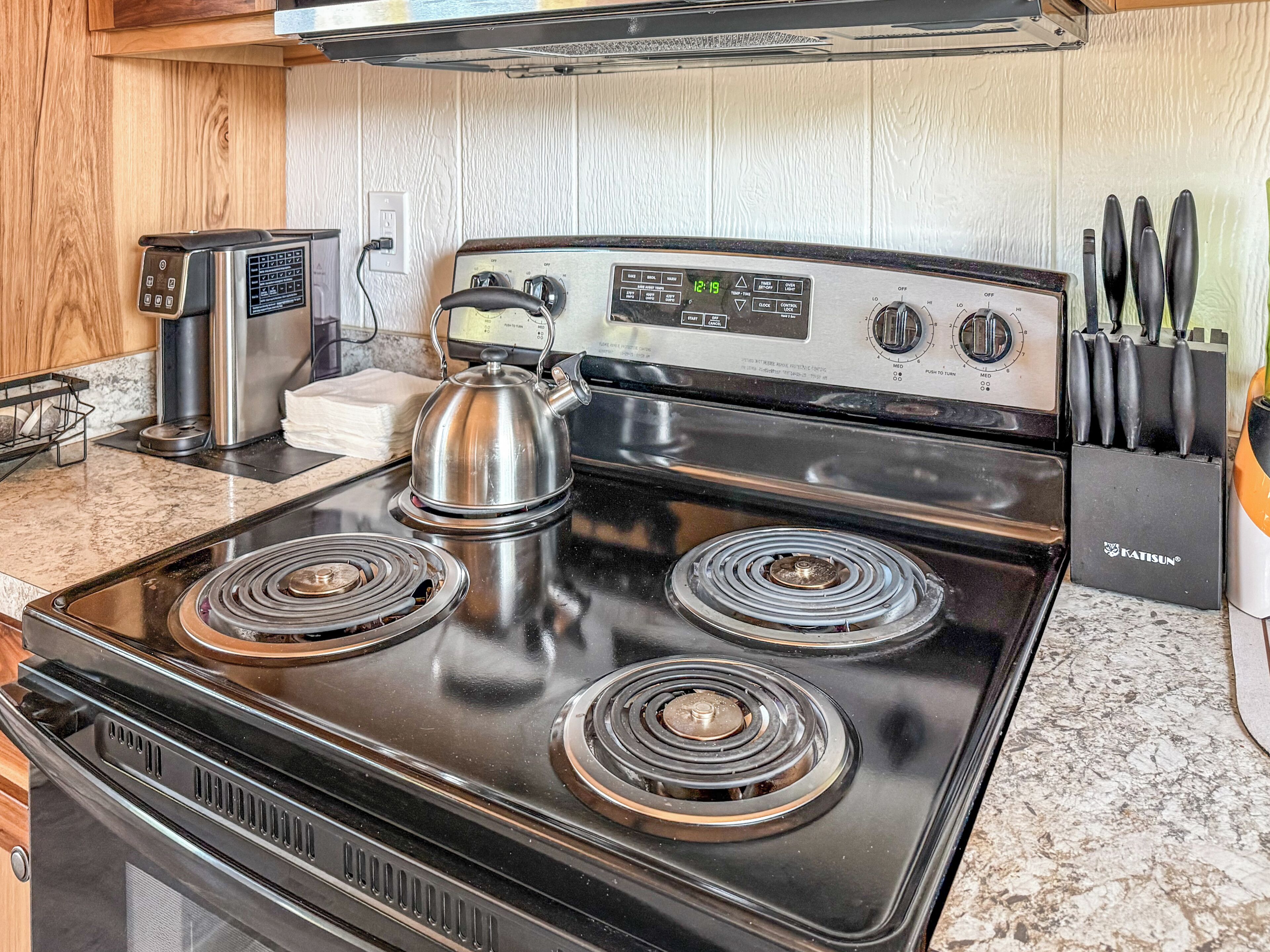 Una cocina con estufa de acero inoxidable, hervidor y bloque de cuchillos.
