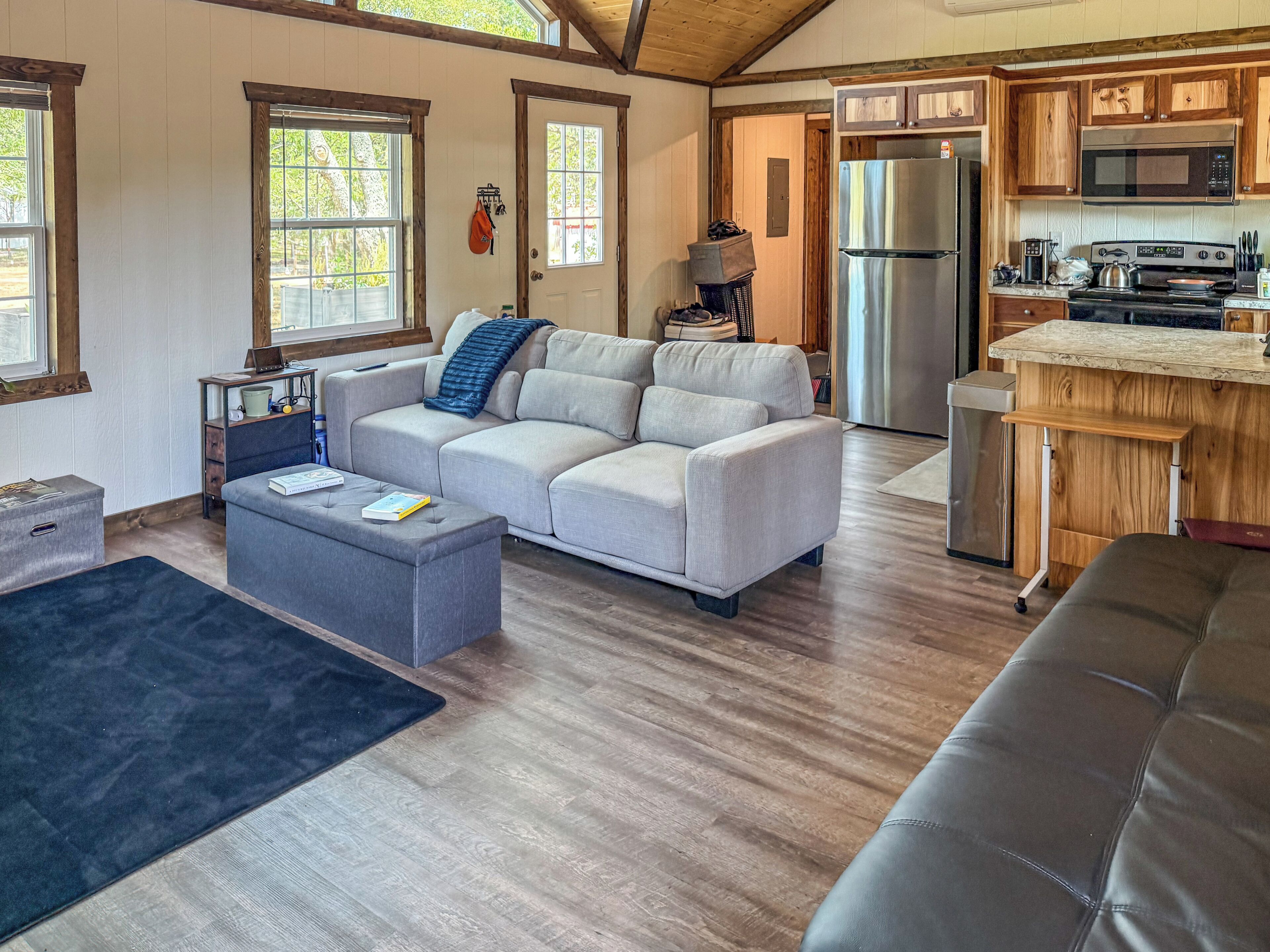 A modern living room with a sectional sofa, a coffee table, and a kitchen area with wooden cabinets and appliances.