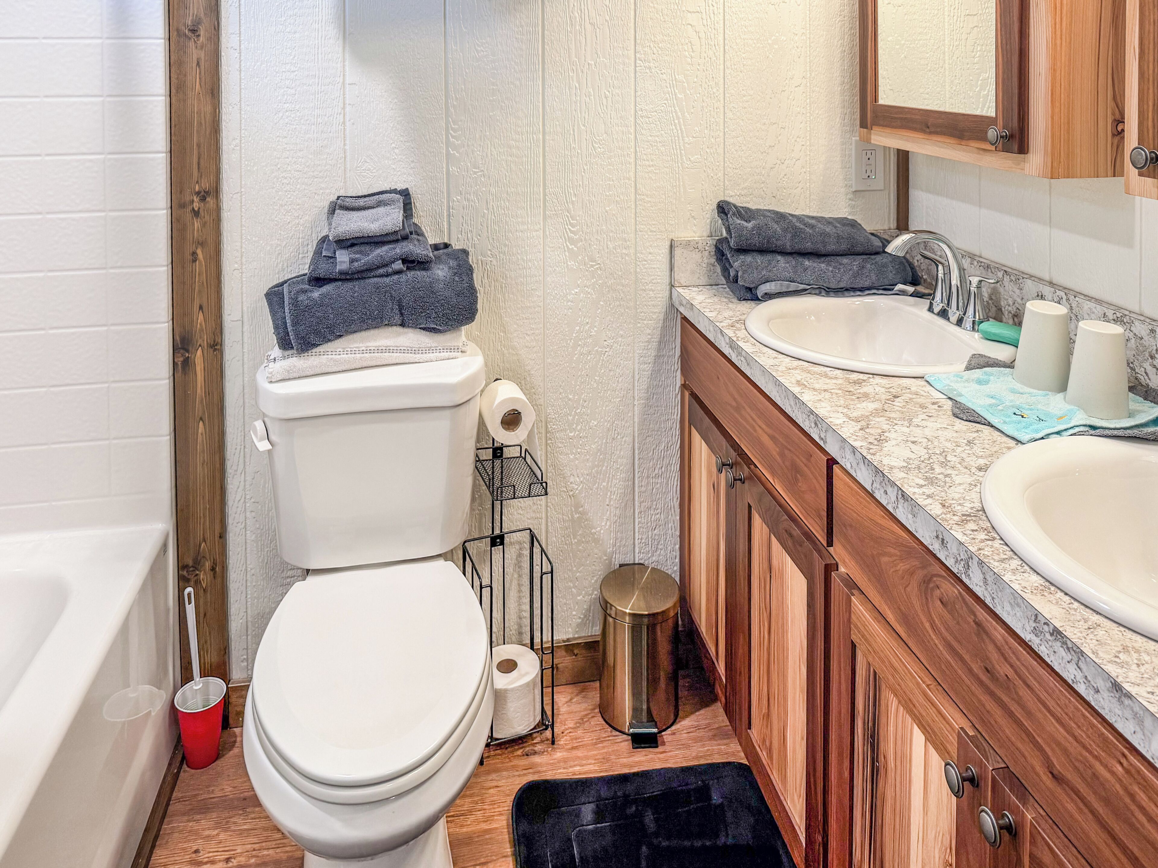 A bathroom with a toilet, two sinks, a trash can, and a wooden cabinet.