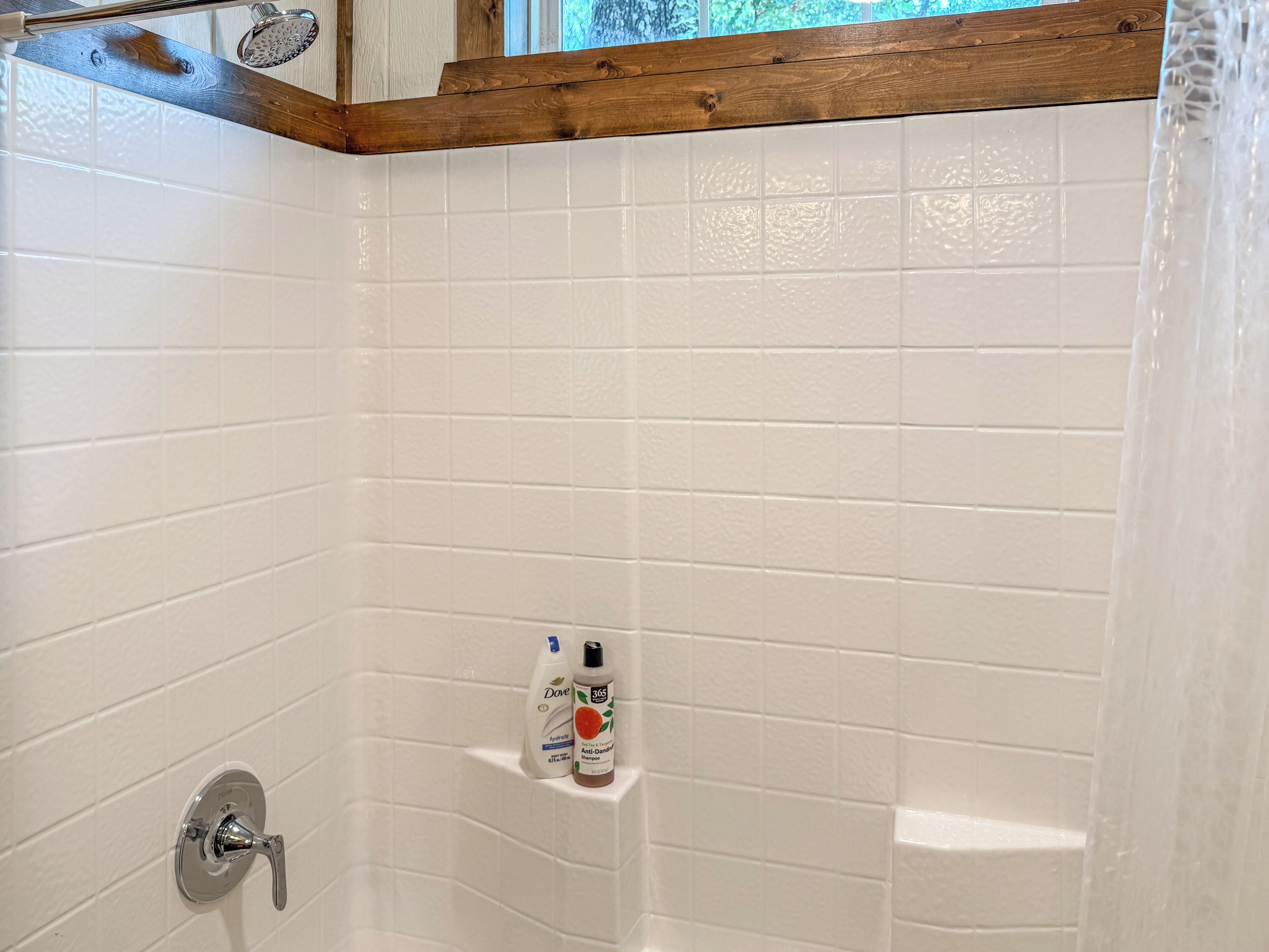 A bathroom with white tiled walls, a wooden ceiling, and a shower area.