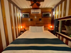 Une chambre d’hôtel avec un grand lit, des lambris en bois sur les murs, deux lampes de chevet et un appareil de climatisation placé au-dessus du lit.