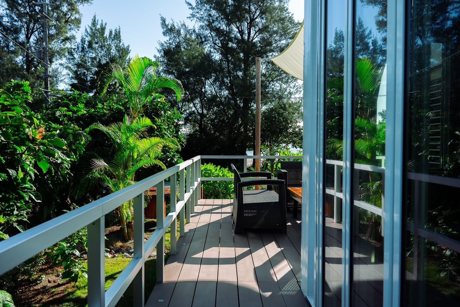 A wooden deck with a white railing, surrounded by lush greenery and trees.