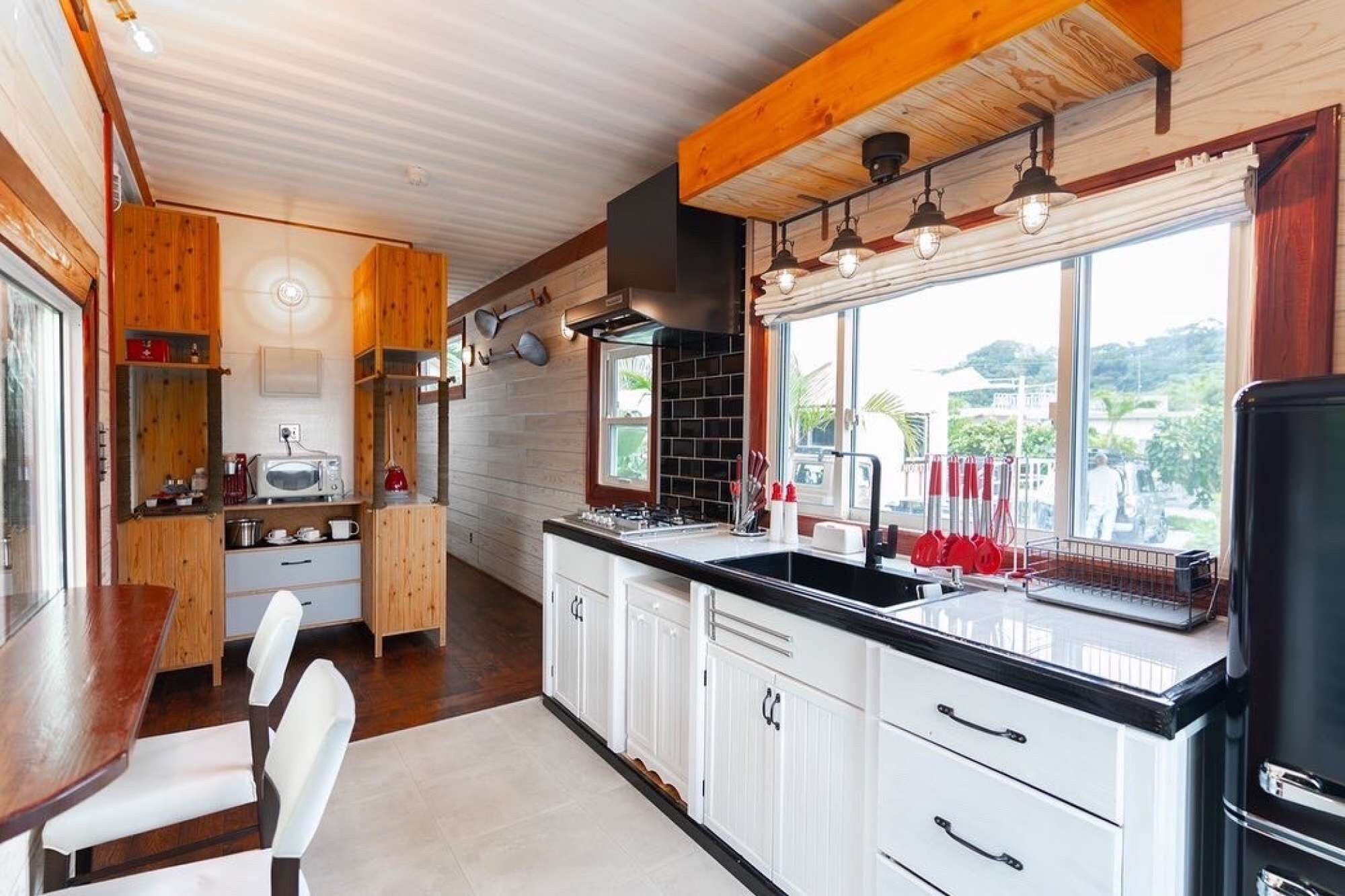 A modern kitchen with wooden cabinets, a black countertop, and a large window offering a view of the outdoors.