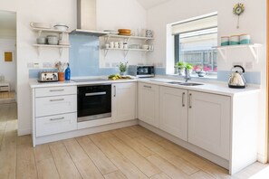 A modern kitchen with white cabinets, a built-in oven, a microwave, and a window providing natural light. - An Mordros - sleeps 6 guests  in 3 bedrooms (Hayle)