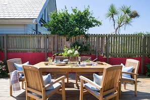 A wooden deck with a table set for dining, surrounded by chairs with cushions. - An Mordros - sleeps 6 guests  in 3 bedrooms (Hayle)
