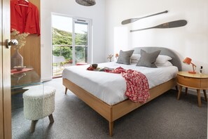 Une chambre à coucher comprenant un lit, des tables de chevet, une commode, une fenêtre avec vue et une porte.