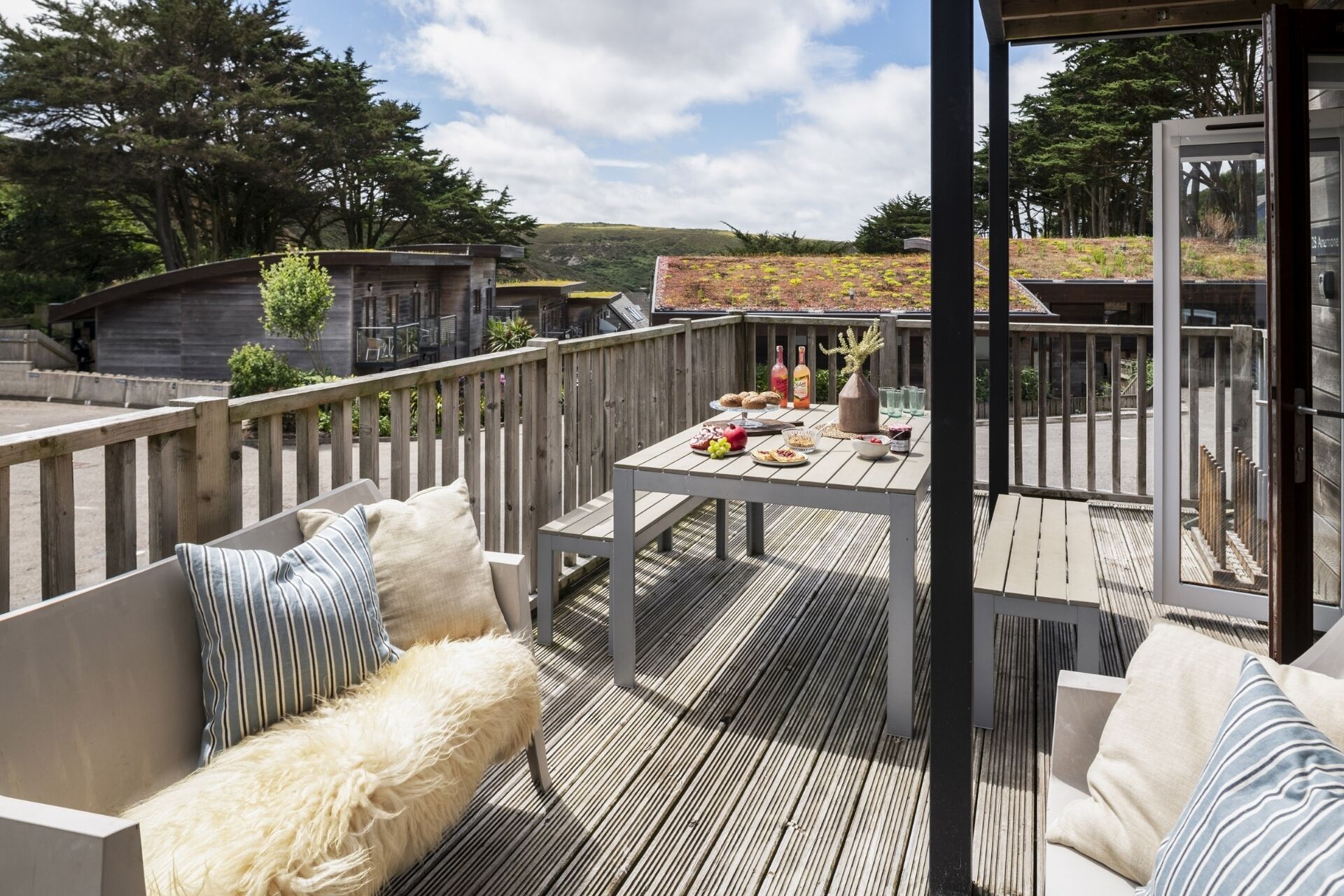 An outdoor deck with a table set for dining, surrounded by wooden railings and furnished with a sofa and cushions.