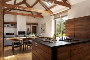 A modern kitchen with wooden beams, a large island, and a view of the outdoors. - Avallen Barn - sleeps 8 guests  in 4 bedrooms (Helford)