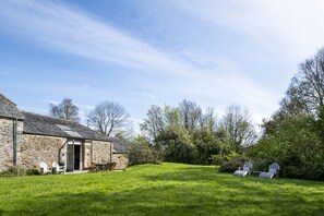 A stone building with a door and windows, a grassy lawn, and Adirondack chairs. - Avallen Barn - sleeps 8 guests  in 4 bedrooms (Helford)