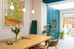 A dining area with a wooden table, chairs, a map on the wall, and a blue cabinet. - BeachSpace - sleeps 8 guests  in 4 bedrooms (Newquay)