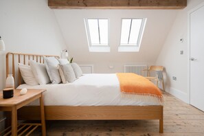 A bedroom with a wooden bed, white bedding, a small table with a lamp, and two windows. - BeachSpace - sleeps 8 guests  in 4 bedrooms (Newquay)
