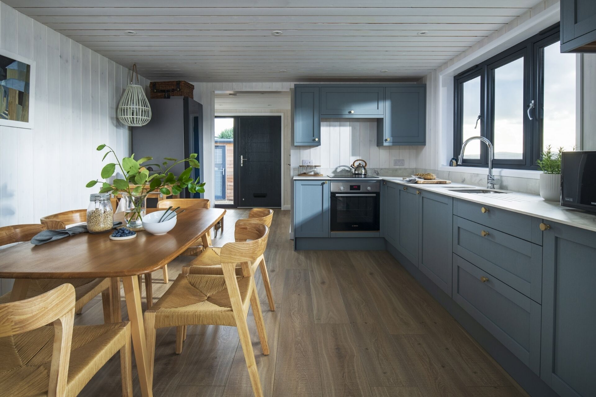 A modern kitchen with wooden flooring, a dining area with a wooden table and chairs, and blue cabinets.