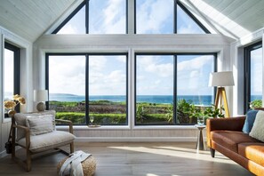 A room with a large bay window overlooking a coastal landscape, furnished with a sofa, a chair, and a small table. - Blue Haze - sleeps 6 guests  in 3 bedrooms (Hayle)