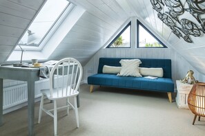 A room with a sloped ceiling, a blue sofa, a white chair, and a table with a lamp. - Blue Haze - sleeps 6 guests  in 3 bedrooms (Hayle)