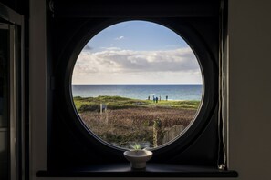 A round window with a view of a grassy area and the sea. - Blue Haze - sleeps 6 guests  in 3 bedrooms (Hayle)