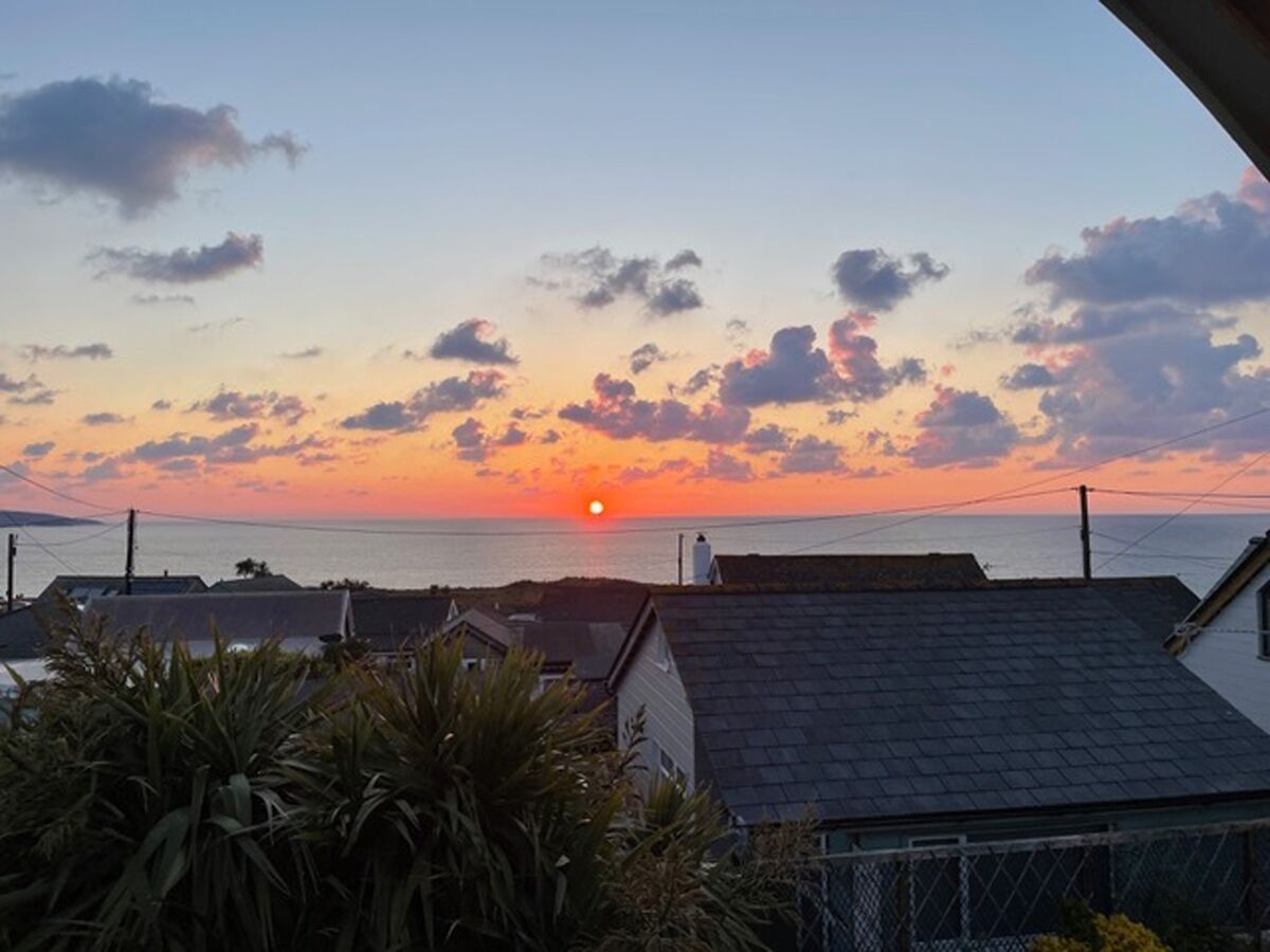 Un coucher de soleil sur une zone côtière, avec des bâtiments et de la végétation au premier plan.