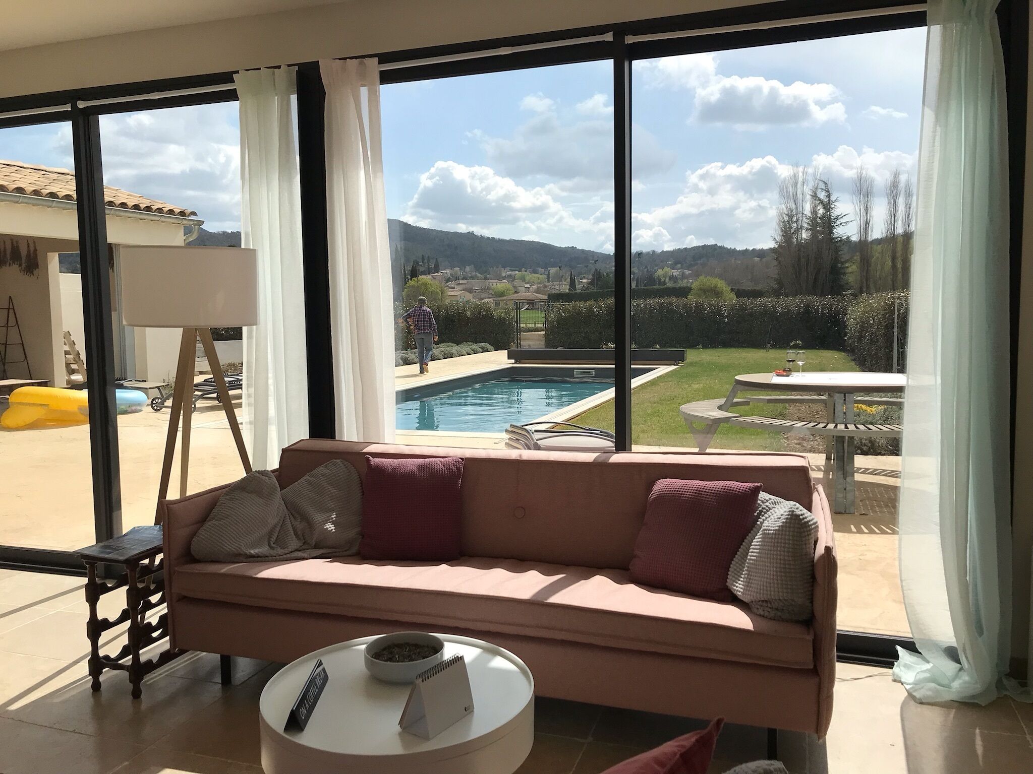 A living room with a sofa, a coffee table, and a view of a swimming pool and garden.