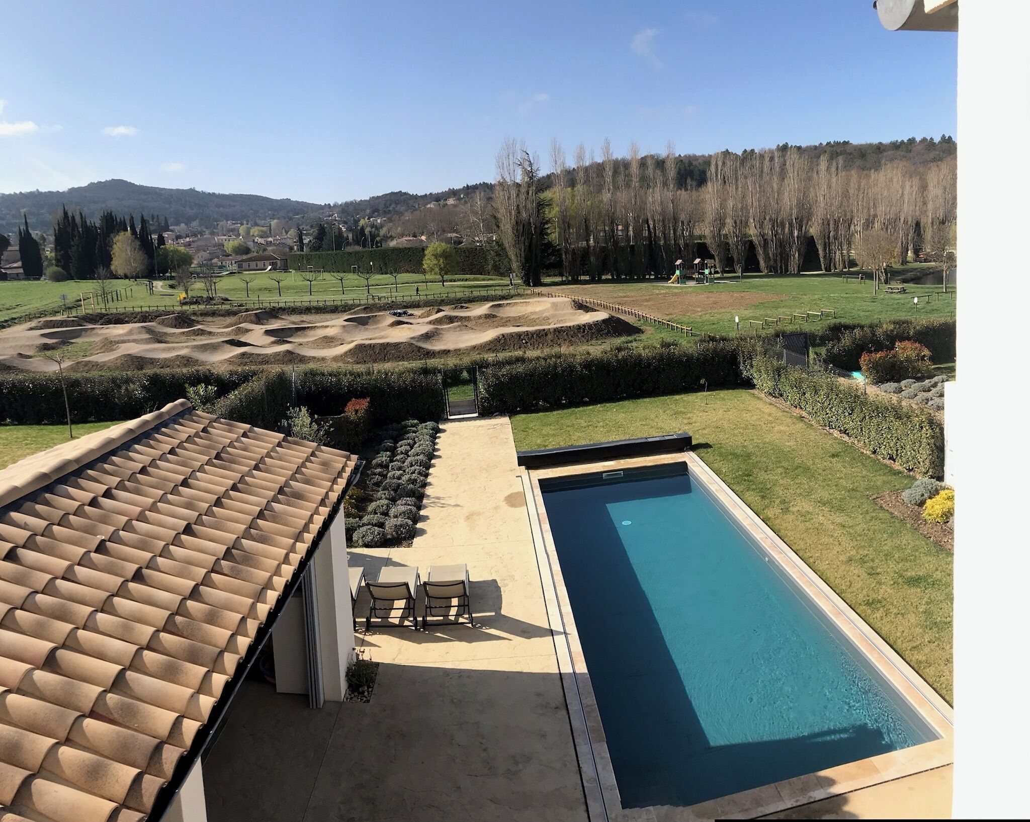 A residential property with a swimming pool, a patio with chairs, and a landscaped garden.