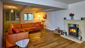 A cozy living room with a sofa, a small table, a fireplace, and a bookshelf. - The Cottages Collection at Rusty Lane Farm (Seend)